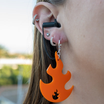 Close-up of a person's ear wearing multiple piercings and a bright orange flame-shaped dangle earring with earplugs attached for concerts